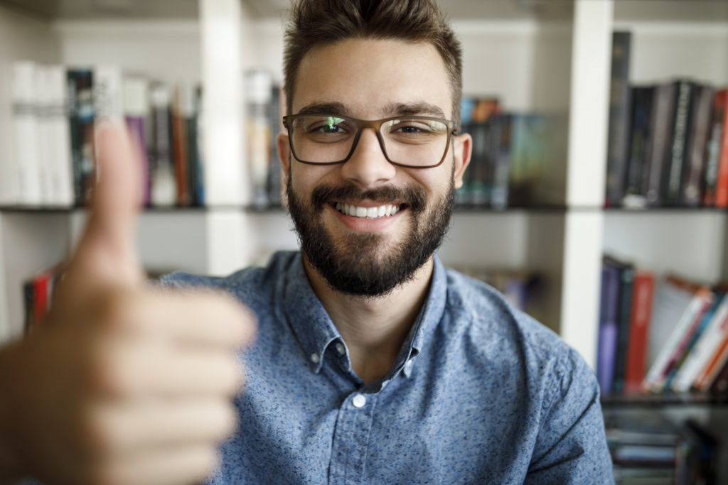 Camera point of view of young man holding thumbs up at home office