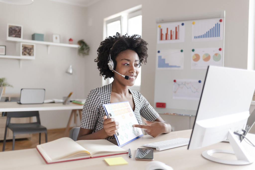 Black Female Employee Sit at Desk in Office Talk on Video Call With Client, Smiling Young Businesswoman Have Webcam Conference at Workplace, Virtual Event Concept