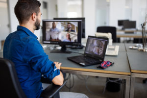 Businessman video conferencing with team on computer. Young man discussing project details with team via video call.