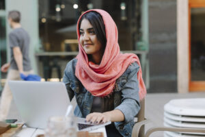 Smiling young woman with laptop wearing headscarf at a pavement cafe