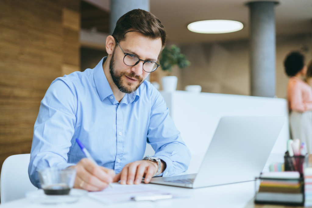 A business man is busy typing on his laptop with focused attention, demonstrating productivity in a corporate business setting with colleagues in the background