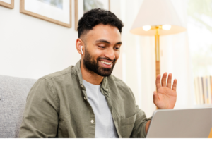 The young adult male sits in his home office to meet virtually with his colleagues during a video call.