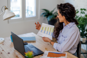 businesswoman with papers having video conference by laptop computer at office