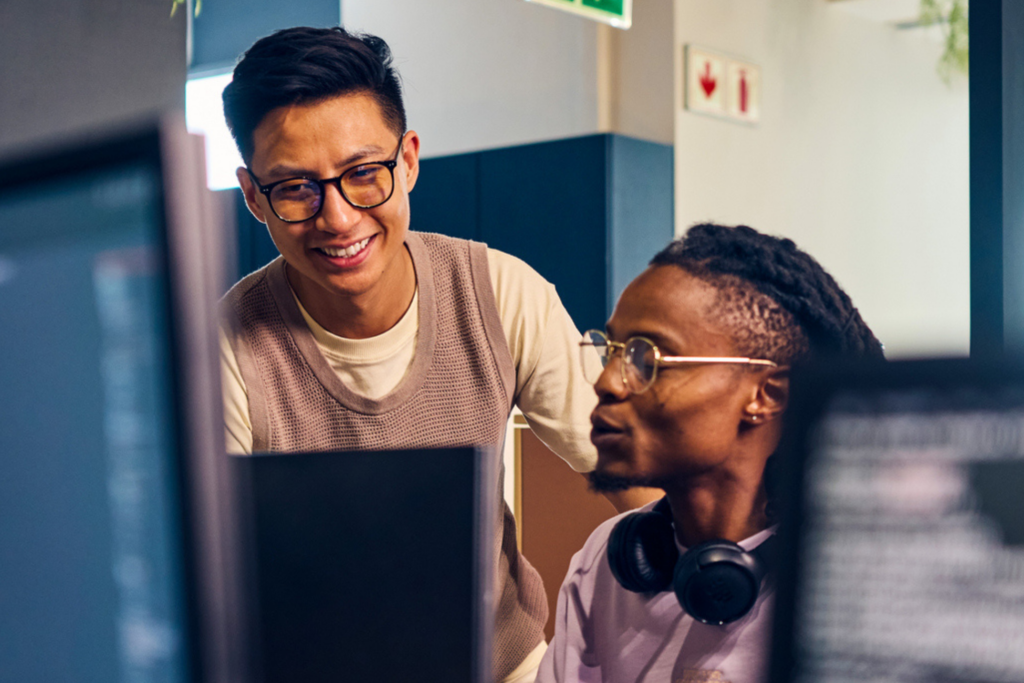 Two diverse software developers collaborating on a project, reviewing code on computer screens in a contemporary office space