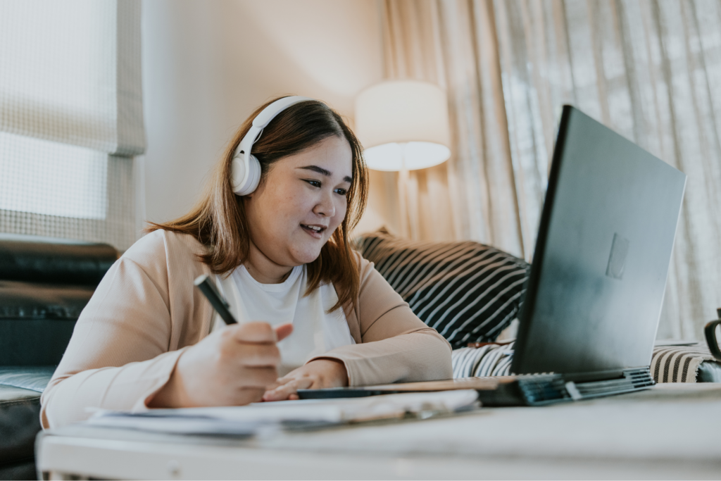 Woman sits on the floor in front of her couch, smiling, navigating on laptop