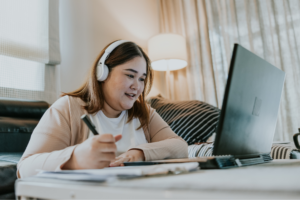 Woman sits on the floor in front of her couch, smiling, navigating on laptop