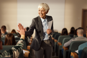 Happy senior professor giving high-five to her college student on a class in a lecture hall.