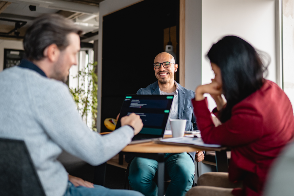 Man smiles as he discusses work with two colleagues at a table