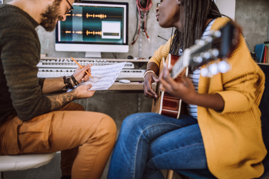 Woman playing acoustic guitar, man writing notes on paper in music studio