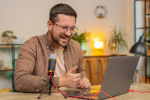 Happy excited blogger man recording podcast at desk, giving workshop, webinar.