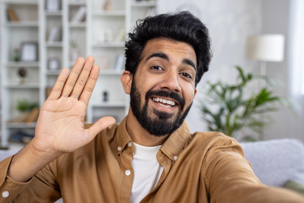 Camera view of positive young man looking at camera and say hello talking by online video call with family or friends at home