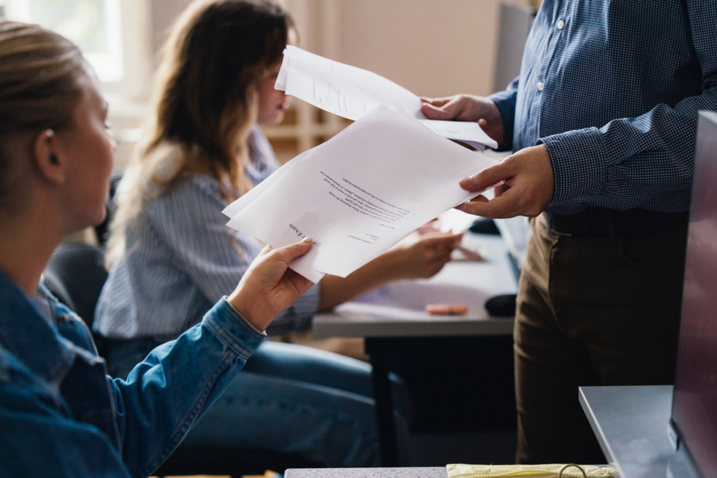 Close up of a teacher handing out exam papers to students in a classroom.
