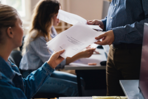 Close up of a teacher handing out exam papers to students in a classroom.