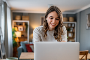 Young woman smiling, confidently working on a laptop at home, embracing remote work and online communication