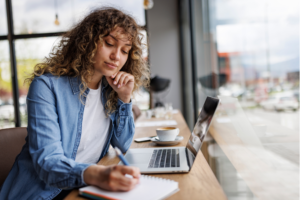 Young woman working on laptop and taking notes at a cafe