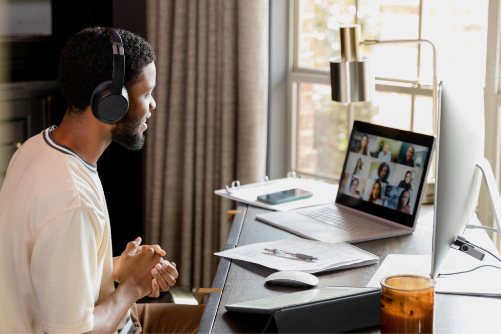 The young adult male college student sits at his home office desk and leads a meeting with his class group