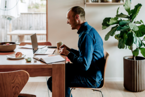 Side view of smiling businessman talking on video call through laptop while sitting near dining table in living room