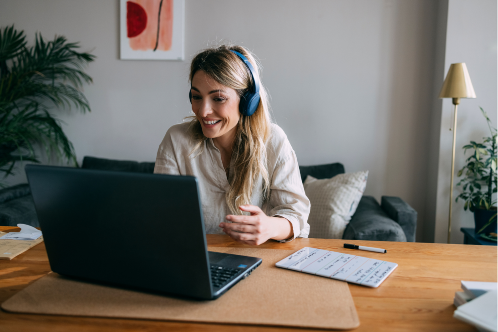 Smiling business woman sitting at table and discuss with clients or coworkers at online web conference using a laptop computer and headphones in a living room