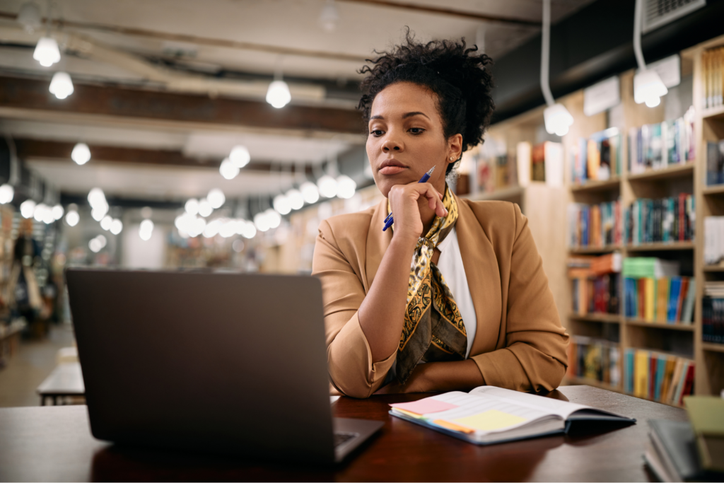 African American female professor using laptop while doing research at university library.