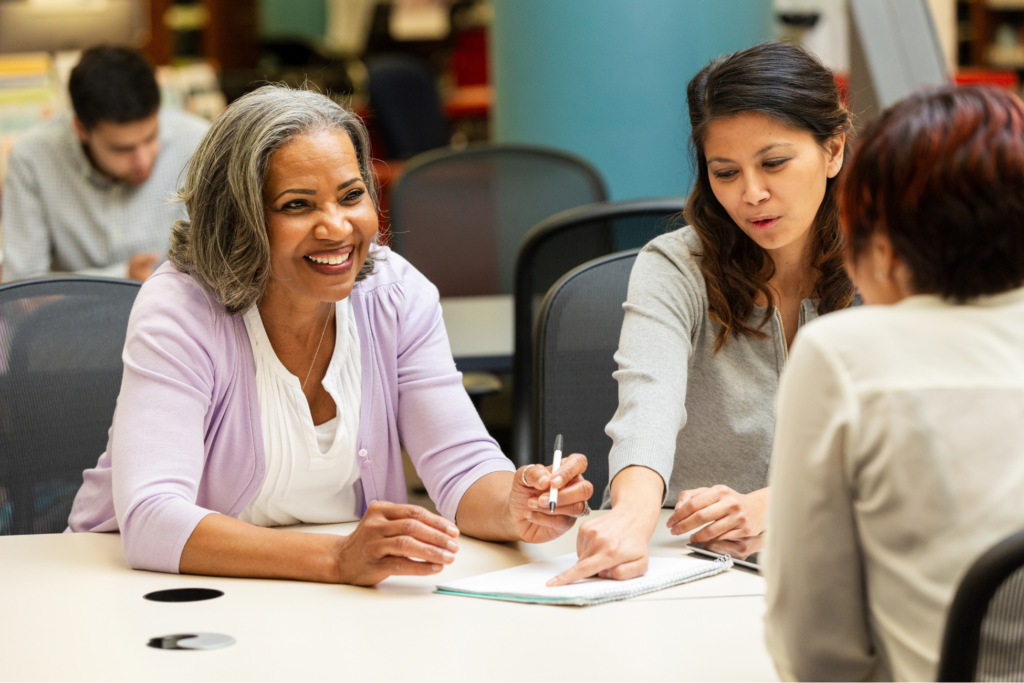 Diverse group of women in an indoor setting actively collaborating and engaged in conversation during a meeting.