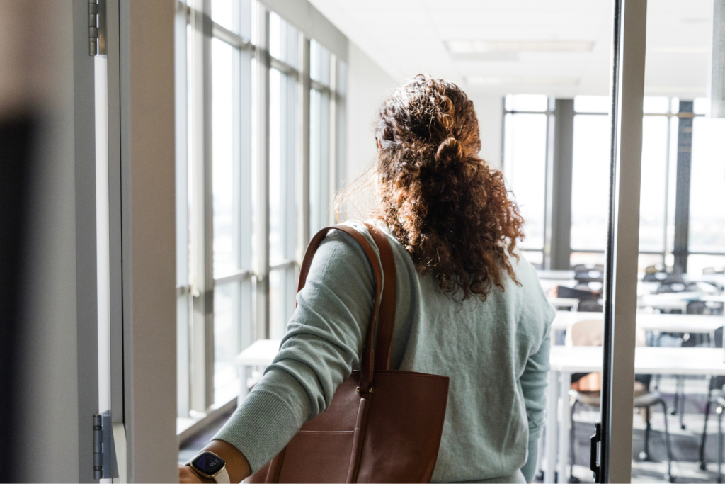 A rear view of a female professor holding the door as she enters her empty classroom before her students arrive.