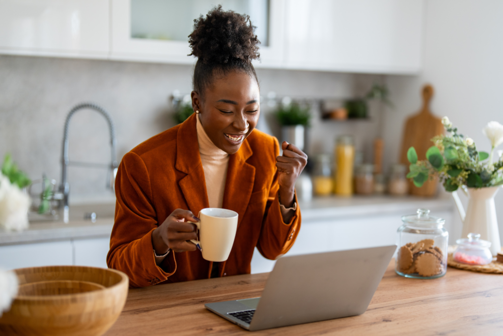 Successful African businesswoman looking at laptop screen celebrating new business opportunity pumping fist while expressing joy.