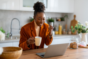 Successful African businesswoman looking at laptop screen celebrating new business opportunity pumping fist while expressing joy.