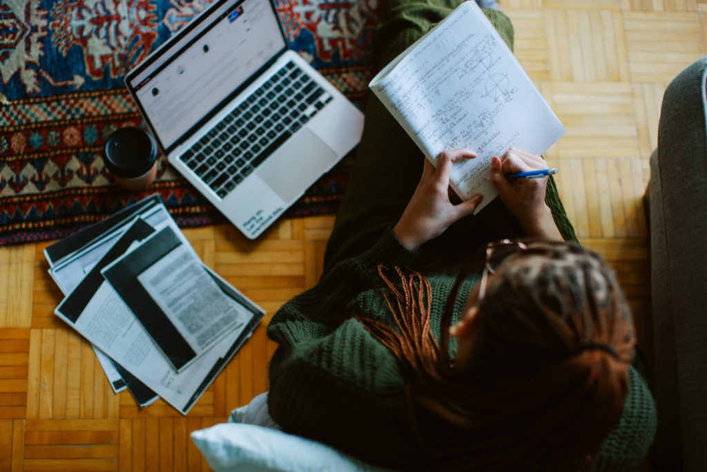 Female student focused on her studies at home, using a laptop and notes in a well-lit and modern apartment in New York.