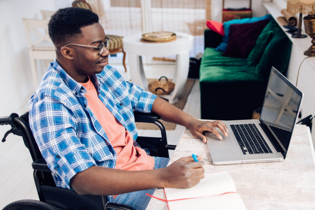 Black male wheelchair user takes notes while navigating on laptop