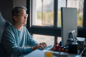 mature man work from home typing and looking at computer at his home office
