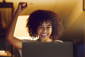 Shot of a young businesswoman cheering while using a laptop during a late night at work