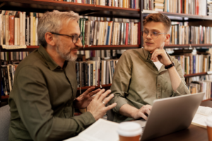 Young male university student talking with university male professor at library or book store