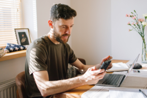 A young military man in uniform sits at his kitchen table, using his smartphone to manage his finances