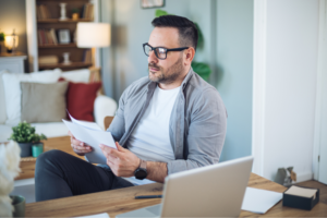 A professor grades papers at his laptop in his home office