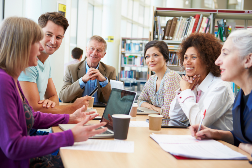 Group Of Mature Students Collaborating On Project In Library With Laptops Smiling