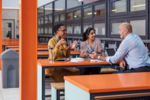 A shot of a small group of teachers discussing their work, wearing smart-casual clothing, sitting in a common area within a secondary school in Gateshead, England.