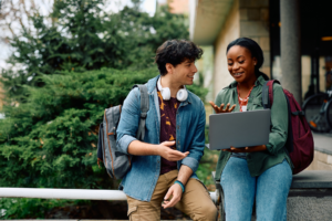 Happy university students e-learning while using laptop at campus.